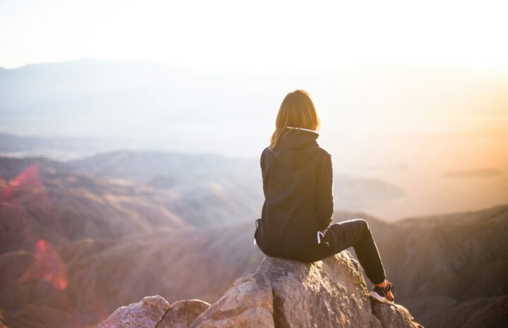 person sitting on top of gray rock overlooking mountain during daytime